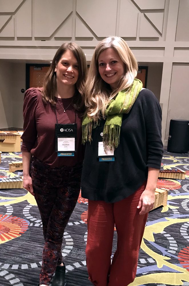 Beth Brown and Diana Hawley standing together in a conference hall, presenter badges on, xylophones on the floor behind them